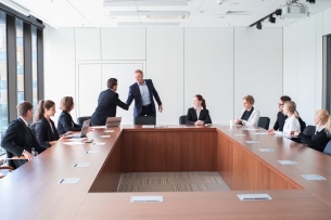 Man shakes the hand of another at a board meeting of men and women