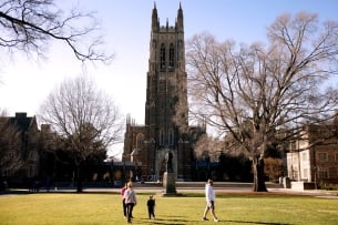 Students walk in front of a chapel tower on the Duke campus
