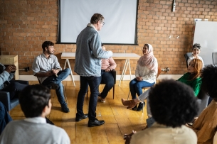 A professor stands in the middle of a circle of students, giving a lesson. 