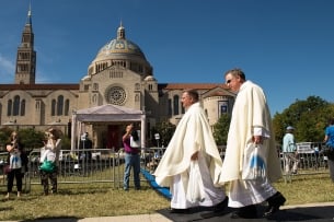 Two clergymen walk in front of the National Shrine of the Immaculate Conception and the Catholic University of America campus.