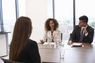 Young woman sitting across table from two people interviewing her for job