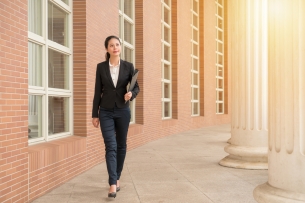 Woman holding business folder walking beside a brick building with colonnade