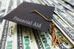 A graduation cap with the words "Financial Aid" sits atop a pile of $100 bills.