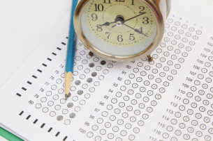 A standardized test answer sheet with bubbles filled in. A pencil and a small circular clock sit atop the sheet.