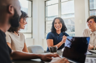 Group of young people smiling as they work together at a desk.