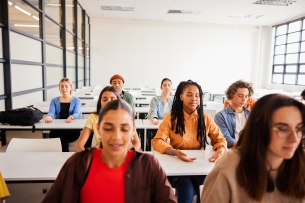 A group of students sit at desks, hands on the desk with eyes closed, practicing mindfulness