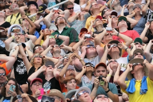 A crowd of people, many of whom are wearing protective eyewear, are looking up at the sky.