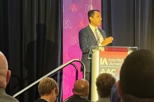 Eboo Patel, founder and president of Interfaith America, stands in front of a podium facing a crowd of campus officials.