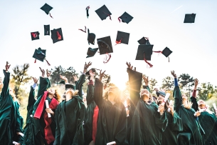Students in graduation gowns throw their caps into the air.