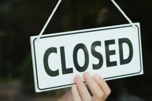 A hand can be seen adjusting a black and white sign that reads “CLOSED.”