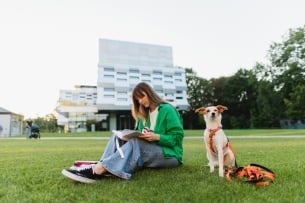 Female student diligently takes notes while her dog keeps her company on her college campus.