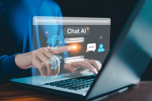 A close-up of human hands resting on a laptop running a chat AI software.