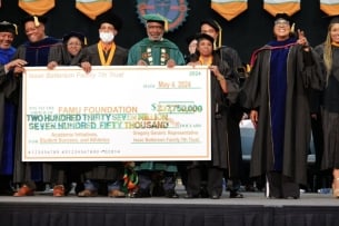 Professors in their ceremonial graduation garb holding a big check on a stage