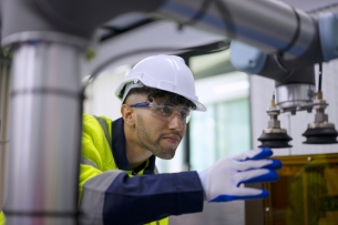 A man in a yellow vest and hard hat examines a machine. 