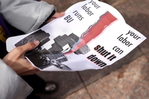 A student holds a flier with the words “your labor runs BU; your labor can shut it down.”