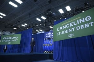 President Biden walks on a stage in front of signs that read “Canceling Student Debt.”