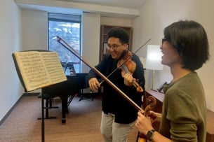 A student plays violin while smiling and looking at sheet music.