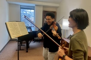 A student plays violin while smiling and looking at sheet music. 