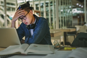 An overwhelmed student sitting in a library staring at his laptop