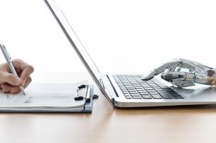 Human hand writing in script while a robot hand types on a laptop