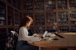 Young woman sits in library writing at a computer