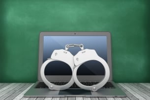 Computer with handcuffs on top of it sits in front of a blackboard