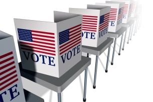 An illustration of a row of empty voting booths, each with an American flag and the word "VOTE," lined up on tables.
