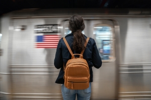 Individual waits on the platform, with a backpack style pocketbook, waiting for the train to stop.