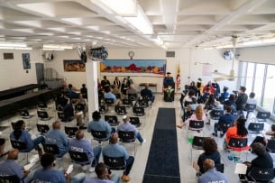 A group of faculty and inmates sit in a large room while Goucher College president Kent Devereaux speaks