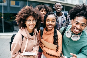 A group of students smile while holding books and backpacks.
