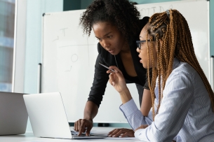 Black woman teacher stands by a student's desk helping her with work