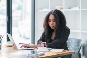 Businesswoman accountant using a calculator, graphs and charts to analyze market data, balance sheets, accounts and net profits in order to plan new sales strategies and increase production capacity
