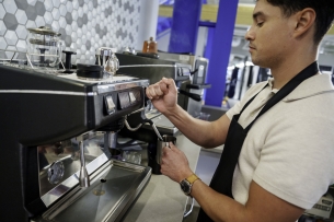 Young Hispanic man in his 20s frothing and steaming milk at a commercial espresso machine