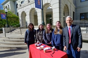 President Alger stands beside four AU students at a table outside on campus