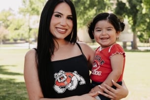A mom and daughter smile in matching Fresno State gear on a sunny day