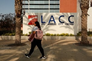 A student walks in front of a sign that reads "Los Angeles City College."