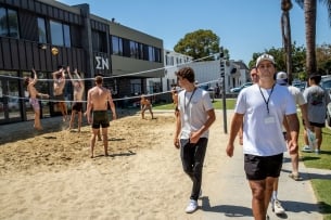 A group of students play volleyball outside of the Sigma Nu fraternity house while others walk on the sidewalk