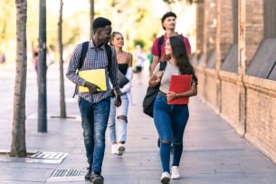 Group of students of different ethnicities walking in the street with school books in summer