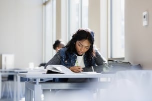 A young woman reads her textbook while taking notes