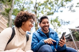 Young man showing something on mobile phone to his friend on stairs outdoors