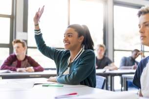 Smiling teenage girl raising hand in classroom
