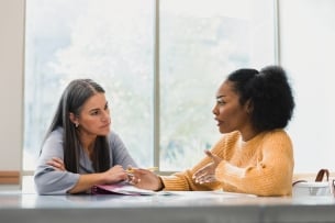 A student speaks with a teacher sitting down in a classroom.
