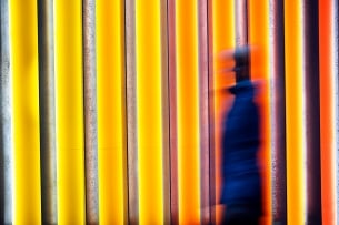 A blurred image of a person positioned toward the center-right of the frame, against a bright orange and yellow background.
