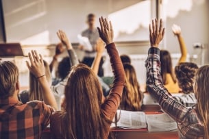 A rear view of a group of students in a lecture hall, raising their hands.