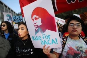 A student in a crowd holds up a sign that reads "Rise for DACA!"