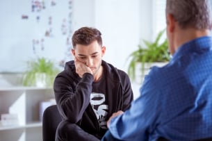 Sad young man discussing with therapist in meeting. 