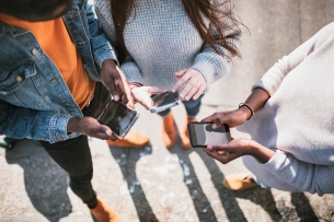 A multiethnic friend group shares things from social media with each other on their various mobile devices. View from above looking down at the phones.