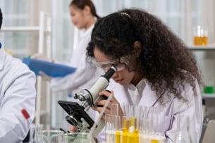 Young scientist with protective eyewear looking through a microscope in laboratory for medical and biological research.