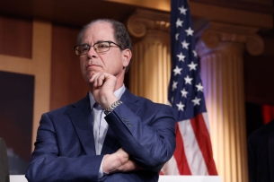 Indiana governor Mike Braun looking into the distance with an American flag behind him. 