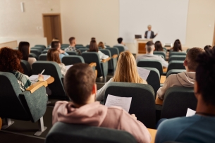 Back view of large group of students paying attention to a class in a lecture hall.
